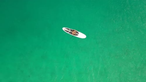 Luftaufnahme einer Frau auf einem weißen Supboard im türkisfarbenen Wasser der Malediven