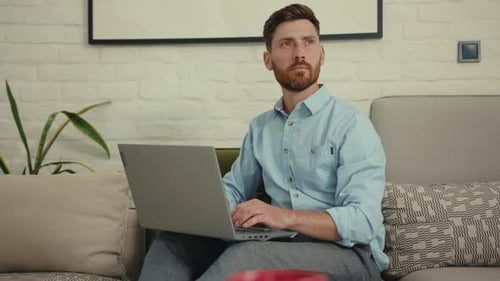 Man Using Laptop on Sofa in Bright Living Room