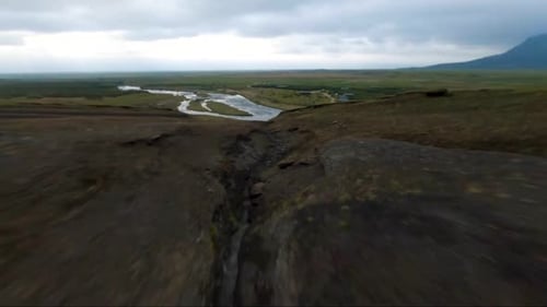 FPV drone dives down a hill alongside a mountain river in Iceland