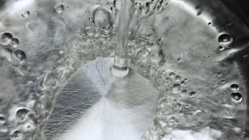 Water is poured into the bottom of a metal pan. Slow motion.