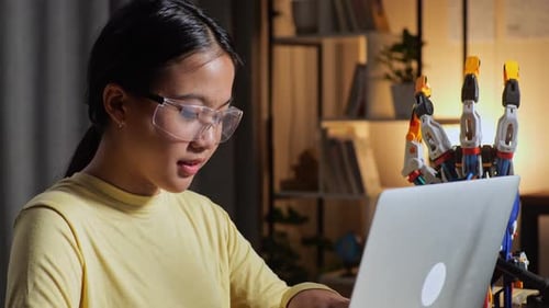 Close Up Of Teen Asian Girl Working About A Cyborg Hand On A Laptop At Home