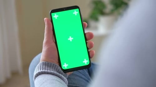Young Man Sitting at Home Holding Smartphone Green Mockup Screen in Hand Male Person Using Chroma