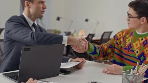 Gerente de Recursos Humanos estrechando la mano de un joven candidato en una entrevista de trabajo con un colega
