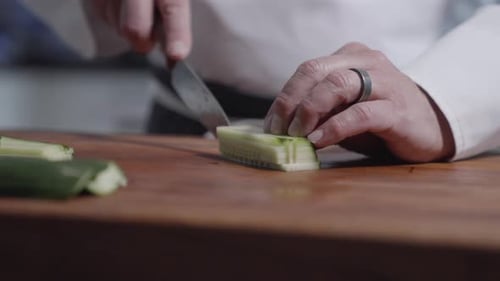 “Close-up shot of chef dicing cucumbers into small squares on wooden cutting board before walking aw
