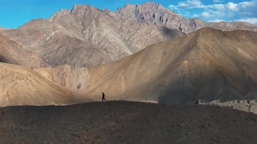 Aerial Drone shot of man running on the top of the cliff of mountain.