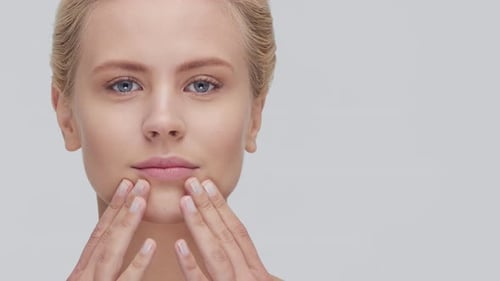 Studio Portrait of Young Beautiful and Natural Blond Woman Applying Skin Care Cream Face Lifting