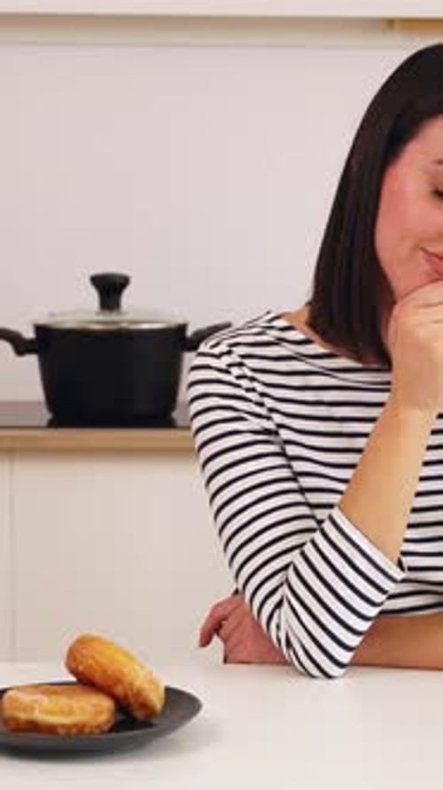 Doubtful Woman Choosing to Eat Healthy Apple or Donuts in the Kitchen