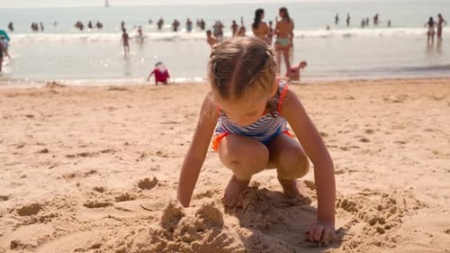Little Girl Builds Sand Castle at Beach on Sunny Day