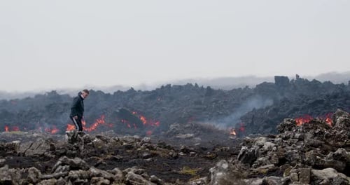 Man walking through a rocky landscape near molten lava flow at Grindavik volcano, Iceland.