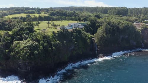 Drone shot of a luxurious private resort on the side of a cliff surrounded by lush green foliage. Be