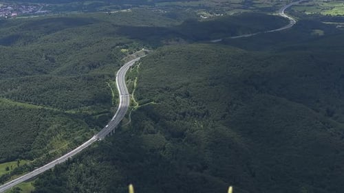 Lange, kurvenreiche Autobahnstraße mitten im Wald, auf der Autos und Lastwagen fahren.