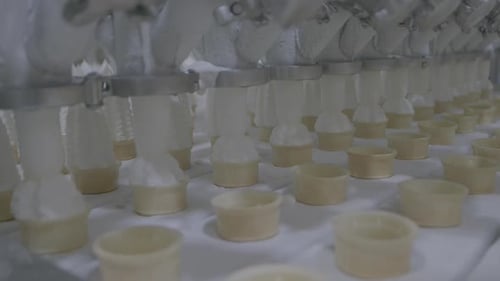 Clip fixe montrant des rangées de cornets de crème glacée remplis d'une cuillère molle à la vanille sur une chaîne de montage