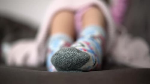 Woman moving feet in winter wool socks, close up, pink blanket