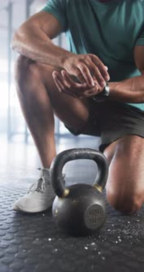 Vertical video: Preparing for workout, man clapping hands with chalk near kettlebell in gym