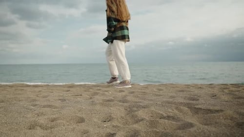 A young woman walks along the beach by the sea in cloudy and windy weather, slow motion. zooms in on