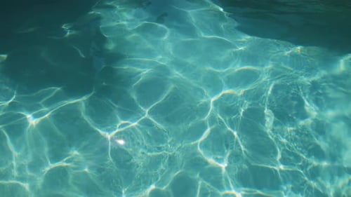 Agua azul transparente de la piscina, destellos solares abstractos en cámara lenta 4K