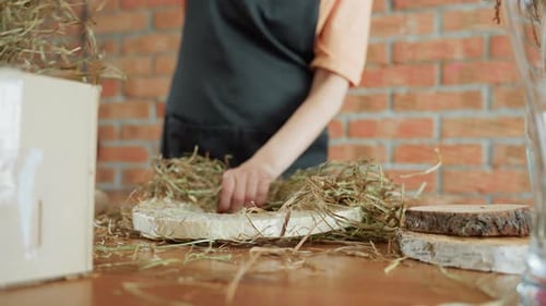 Decorator Arranging Hay Onto Wreath Base on Wooden Table