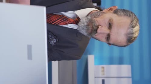 Vertical Video of Mature businessman working on laptop at table in office.