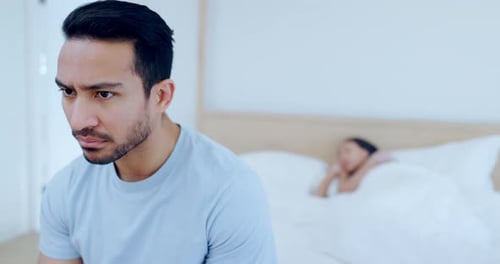 Worried Man Sitting on Bed While Woman Sleeps