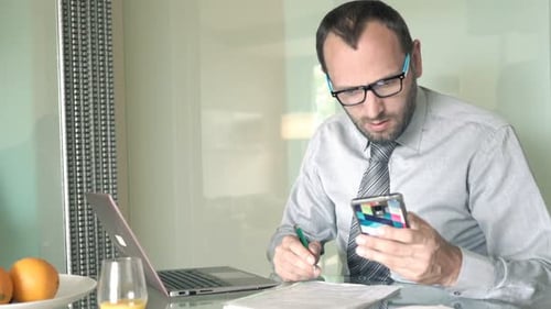 Young caucasian businessman analyzes financials on smartphone at home office