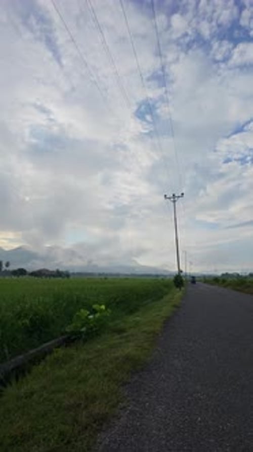 Rural Road With Green Field and Cloudy Sky
