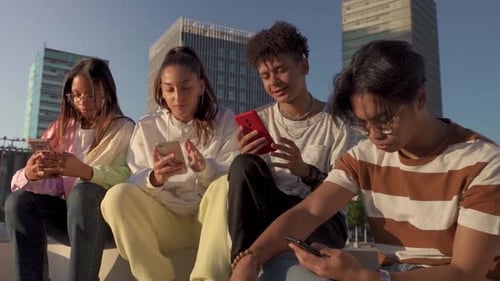 Group of Multicultural Happy Teenage Friends Looking Their Phones in a Bench in the City Street