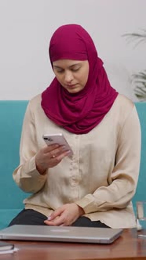 Vertical Video of Muslim Woman in Hijab Scarf Sitting on Couch Texting on Phone