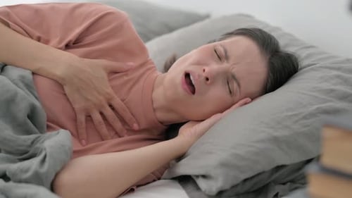 Jeune femme malade tousse en position couchée sur le côté dans son lit