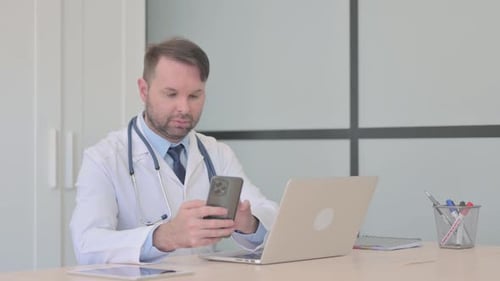 Doctor Using Phone and Laptop in Office
