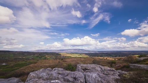 Time lapse of rural landscape with foreground of rocks and grass on hillside and lake in the