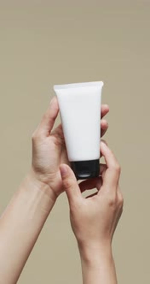 Hands Holding and Displaying White Cosmetic Tube