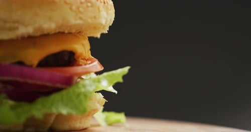 Video close up of cheeseburger with salad in burger bun, on grey background with copy space