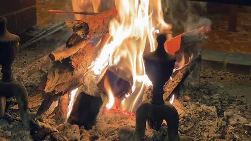 Fire in an open cosy fireplace indoor, in the background chairs on a carpeting, 30 degree angle view