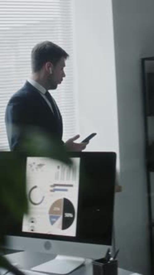 Male CEO Speaking on Phone with Wireless Earphones in Office