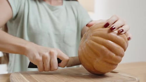 A Woman Cuts a Small Pumpkin in Half. Close-Up on a Wooden Table.