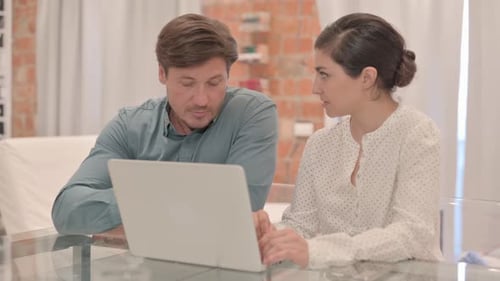 Adults Collaborating at Desk Looking at Laptop