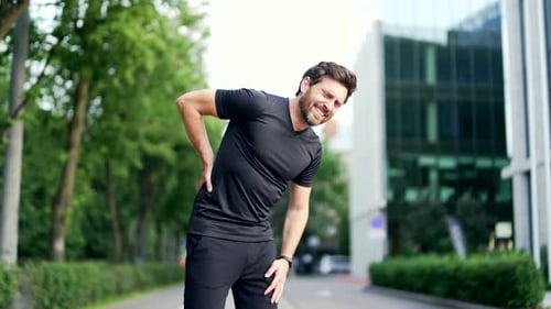 Mature adult runner suffering from back pain, sports injury, muscle spasm in urban city park