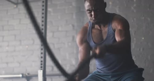 Using battle ropes, muscular man exercising intensely in gym, focusing on workout