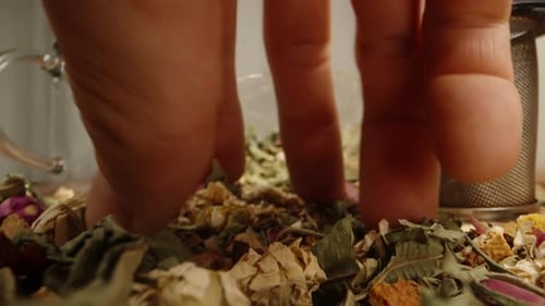 Hands filling tea strainer with dried herbs