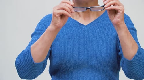 Senior woman puts on eyeglasses in a close-up shot