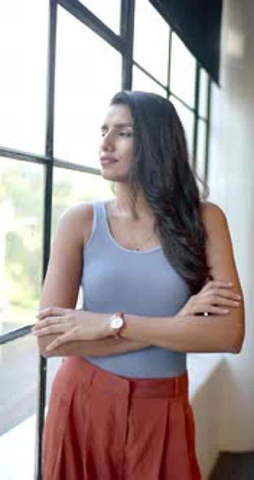 Vertical video: Standing by window, confident businesswoman crossing arms and smiling