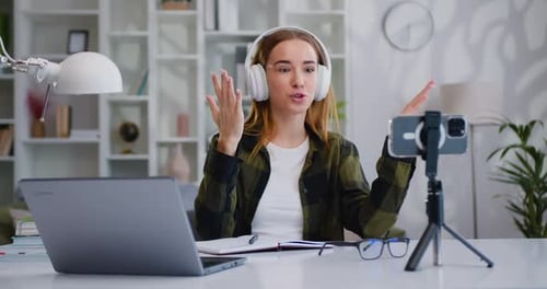 Une influenceuse enregistre un blog vidéo sur un smartphone assise à un bureau à domicile.