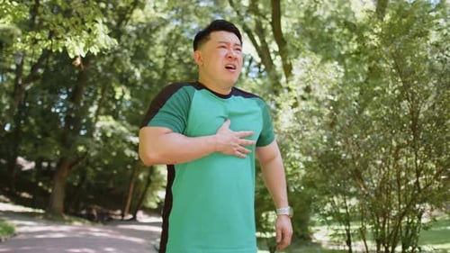 Müder junger erwachsener asiatischer Läufer mit Herzinfarkt oder Brustschmerzen nach dem Lauftraining im Park