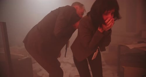 Diverses personnes paniquent dans un bureau en feu alors qu'un pompier s'étouffe et toussent