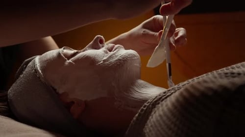 Tratamiento facial relajante de spa con máscara de crema calmante aplicada en el rostro y el cuello de la mujer por un esteticista