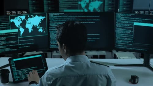 Asiatischer Mann arbeitet mit Tablet, während er Code mit mehreren Computerbildschirmen im Büro schreibt