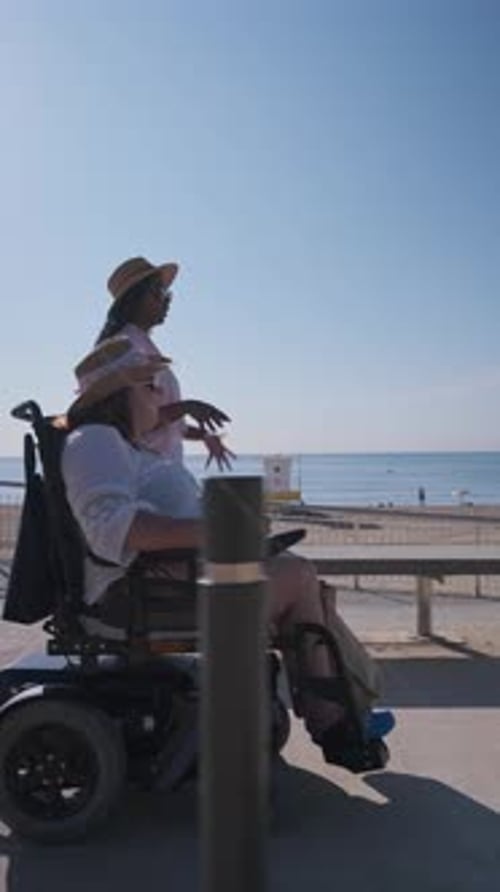 Woman Walking with Friend in Wheelchair By the Sea