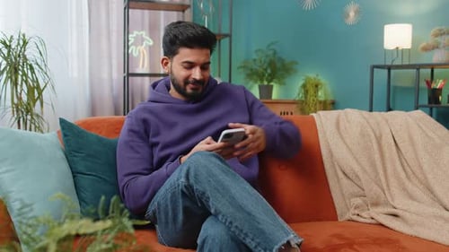 Young Adult Using Smartphone on Orange Sofa