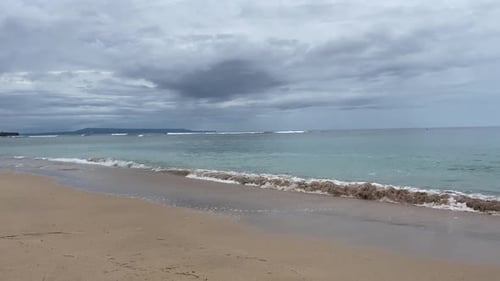 Overcast sky over the ocean, waves hitting a sandy beach.