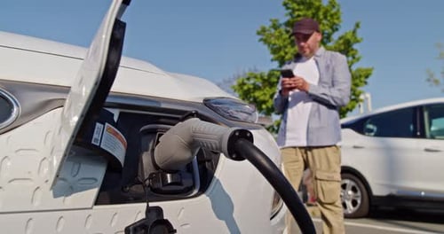 Man Charges an Electric Car at an Electric Charging Station in the City